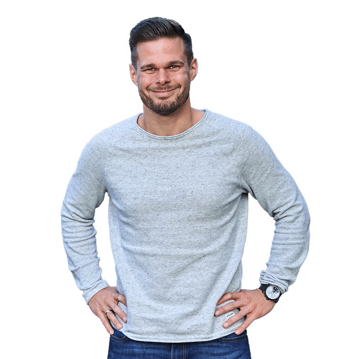 Junger Mann in grauem Shirt stehend lächelnd im Garten, Hände auf der Hüfte