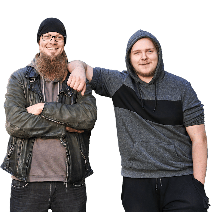 Zwei junge Männer stehen grinsend im Garten, einer im Hoodie, einer mit Mütze