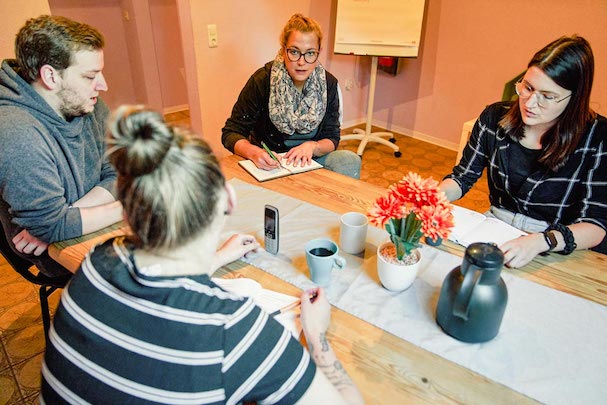 Mitarbeiter*innen beim Meeting am Tisch mit Notizblöcken und Kaffee