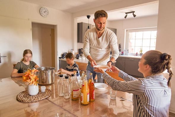 Jugendliche am Esstisch, Mann verteilt Suppe