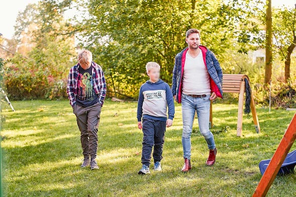 Zwei Jungs und ein Mann spazieren durch den grünen Garten