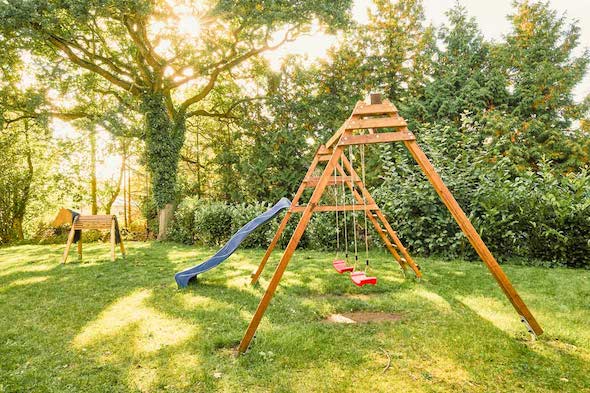 Sonniger, grüner Garten mit Schaukel, Rutsche, Holzpferd